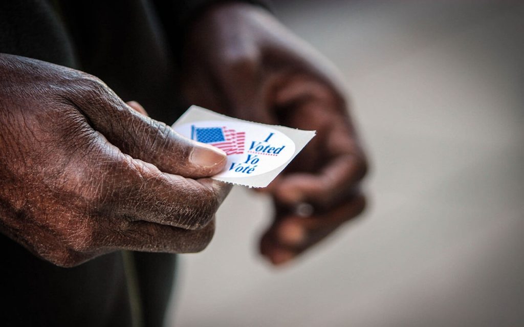 Close-up of a person holding an "I Voted" sticker with an American flag icon.
