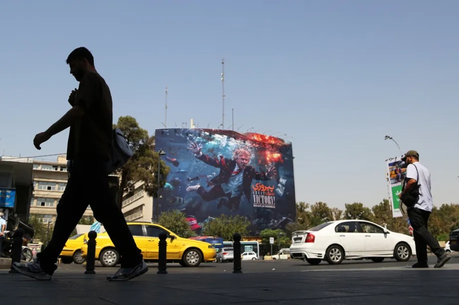 Silhouette of a pedestrian walking past a large urban billboard displaying anti-US artwork in Tehran.