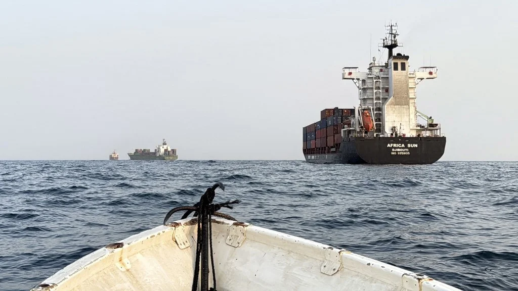 Container ship Africa Sun navigating through open waters with a small boat in the foreground.