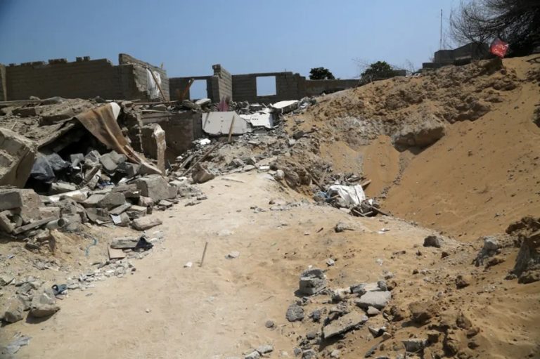 Destroyed buildings and a large bomb crater amid desert rubble