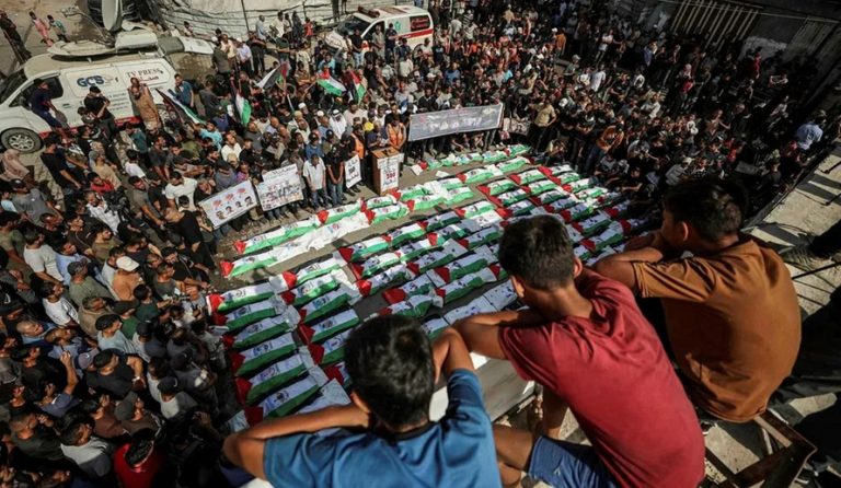Large crowd gathered around bodies wrapped in Palestinian flags during a funeral ceremony in Gaza.