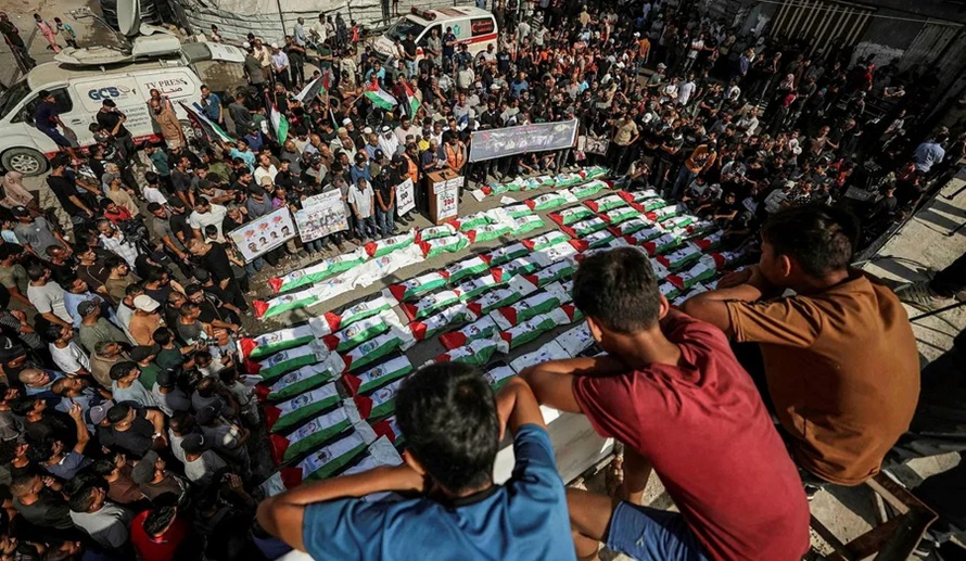 Large crowd gathered around bodies wrapped in Palestinian flags during a funeral ceremony in Gaza.