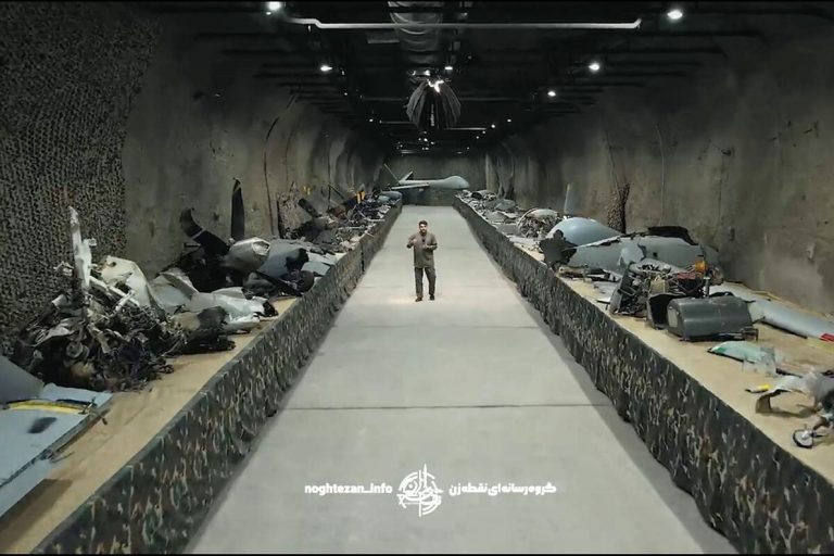 Iranian presenter standing inside an underground tunnel lined with wreckage of downed military drones.