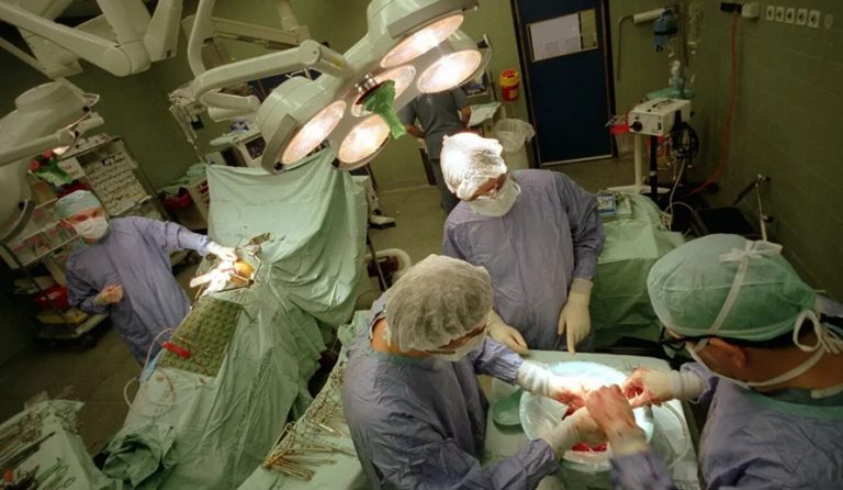 Surgeons in full protective gowns performing an operation in an operating room.