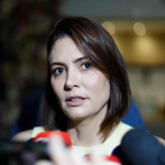 Close-up portrait of Michelle Bolsonaro speaking into microphones at a press conference.