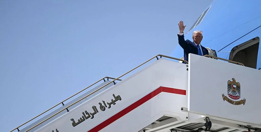 A man waving from the top of an aircraft stairs labeled in Arabic script.