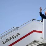 A man waving from the top of an aircraft stairs labeled in Arabic script.