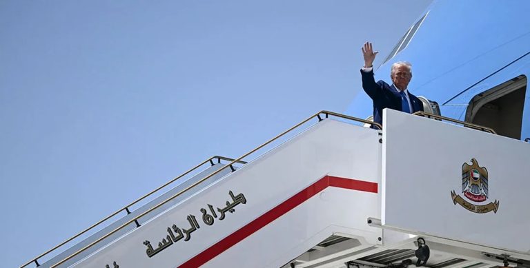 A man waving from the top of an aircraft stairs labeled in Arabic script.