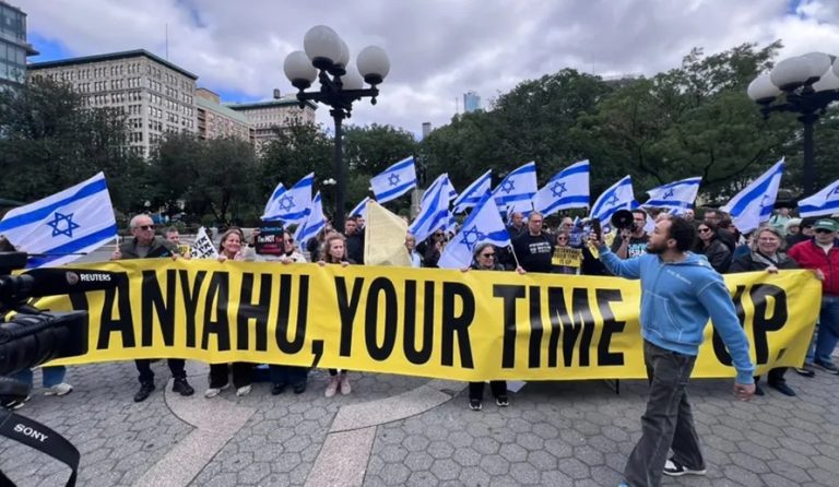 Protesters holding a large yellow banner reading "Netanyahu, Your Time Is Up" surrounded by Israeli flags.