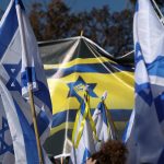 Demonstrators waving Israeli national flags and political banners at an outdoor political rally.