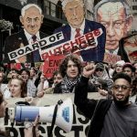 Protesters marching with Palestinian flags, a megaphone, and oversized caricature cutouts depicting political leaders.