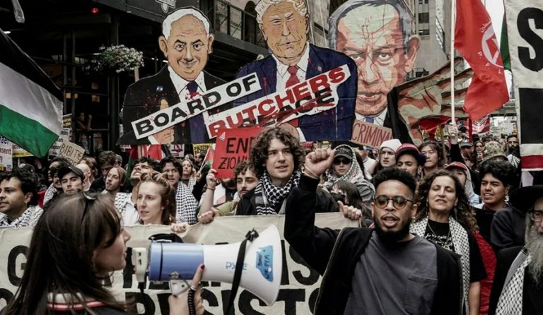 Protesters marching with Palestinian flags, a megaphone, and oversized caricature cutouts depicting political leaders.