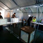 Voters casting ballots in cardboard voting booths set up inside a temporary tent polling place.