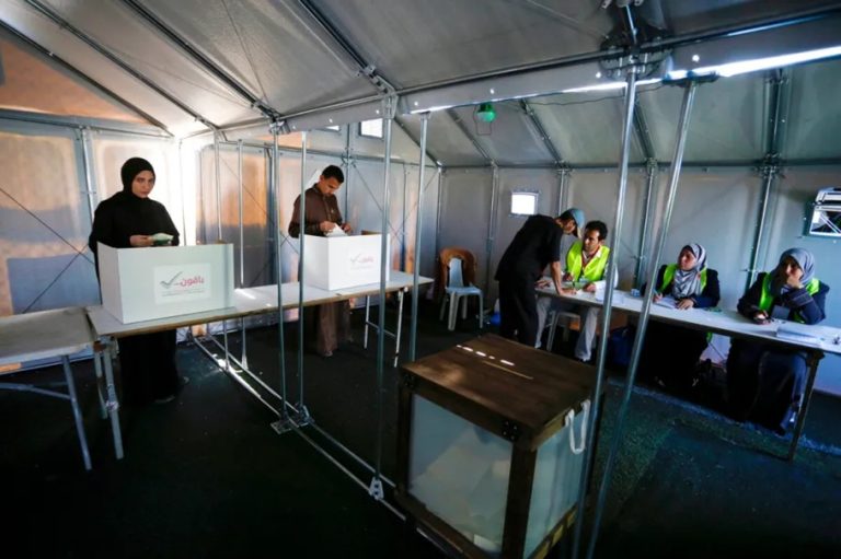 Voters casting ballots in cardboard voting booths set up inside a temporary tent polling place.