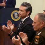 Pete Hegseth clapping alongside military officials during a formal event.