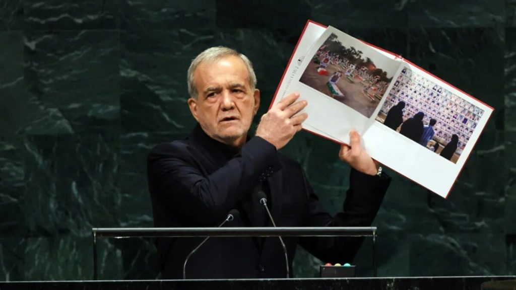 Iranian President Masoud Pezeshkian holding up an open photo book at the UN General Assembly podium.