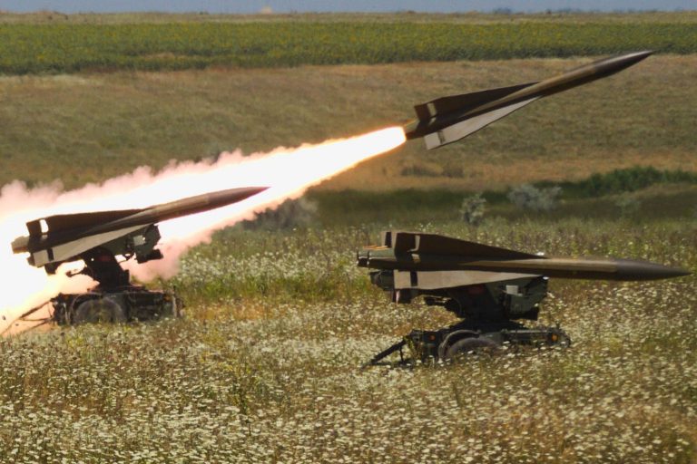Surface-to-air missile launchers firing missiles in a field.