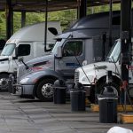 Semi-trucks parked at commercial diesel fuel pumps at a truck stop.