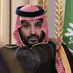 Saudi Crown Prince Mohammed bin Salman seated next to the Saudi Arabian flag.