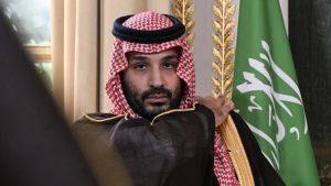 Saudi Crown Prince Mohammed bin Salman seated next to the Saudi Arabian flag.