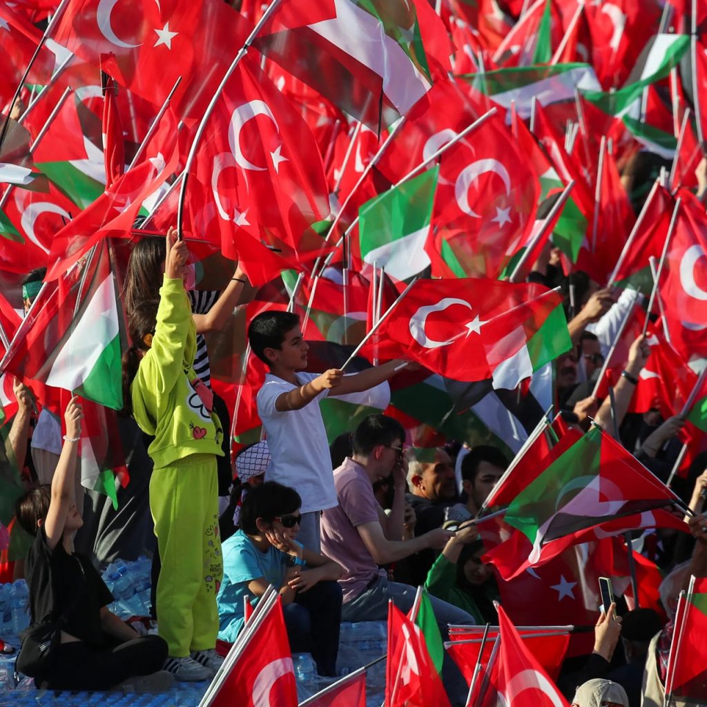 Crowd waving red Turkish flags at a public political rally.