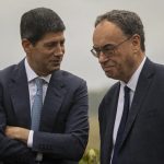 Two central banking officials in dark suits conversing outdoors.
