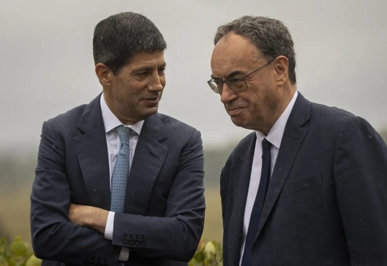 Two central banking officials in dark suits conversing outdoors.