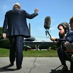 Donald Trump waving as he walks away toward Marine One while journalists point microphones