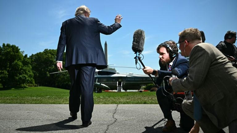 Donald Trump waving as he walks away toward Marine One while journalists point microphones
