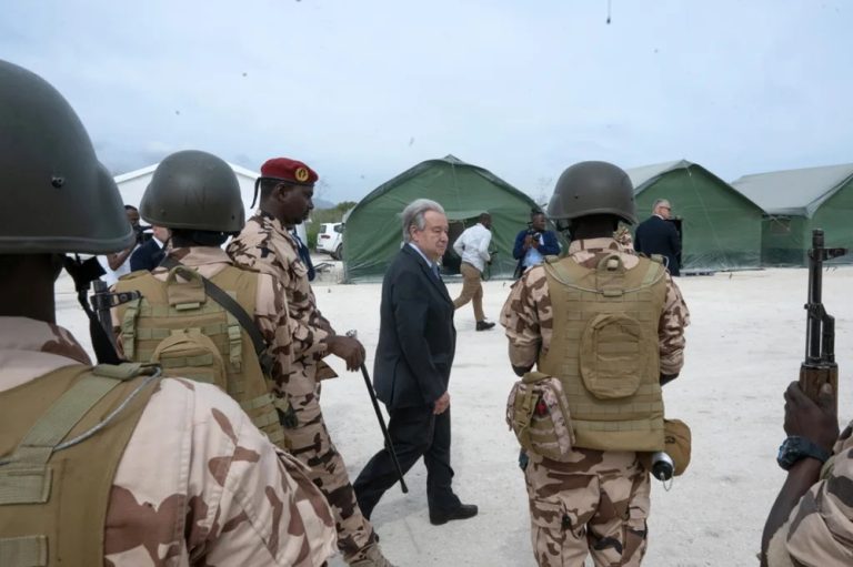 UN Secretary-General António Guterres walking past armed international security personnel at a field site.