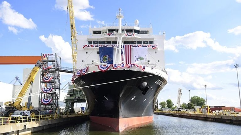Large maritime training and cargo ship docked in a dry dock facility draped with American flags.