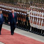 Xi Jinping and Donald Trump walking along a red carpet past a military honor guard.