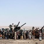 Armed individuals and pickup trucks mounted with anti-aircraft guns in a desert area.