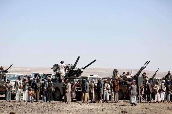 Armed individuals and pickup trucks mounted with anti-aircraft guns in a desert area.