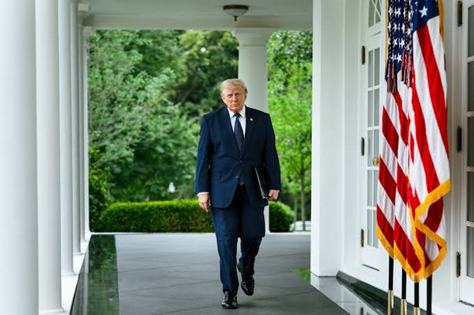 Donald Trump walking along a White House colonnade past American flags.