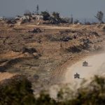 Military vehicles traveling along a dirt road through a damaged terrain landscape.