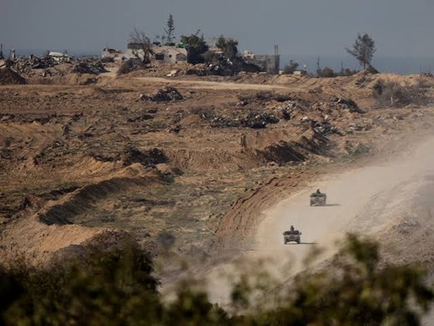 Military vehicles traveling along a dirt road through a damaged terrain landscape.