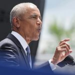 Former U.S. President Barack Obama speaking into a microphone with his hand raised.