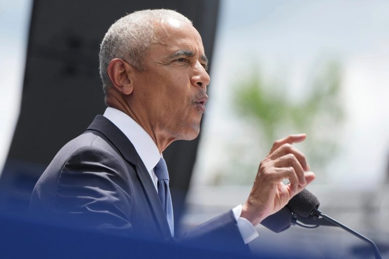 Former U.S. President Barack Obama speaking into a microphone with his hand raised.