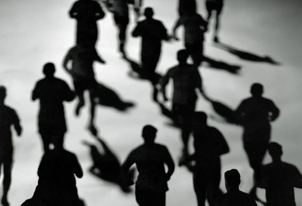 High-angle black and white silhouette of multiple runners moving together.