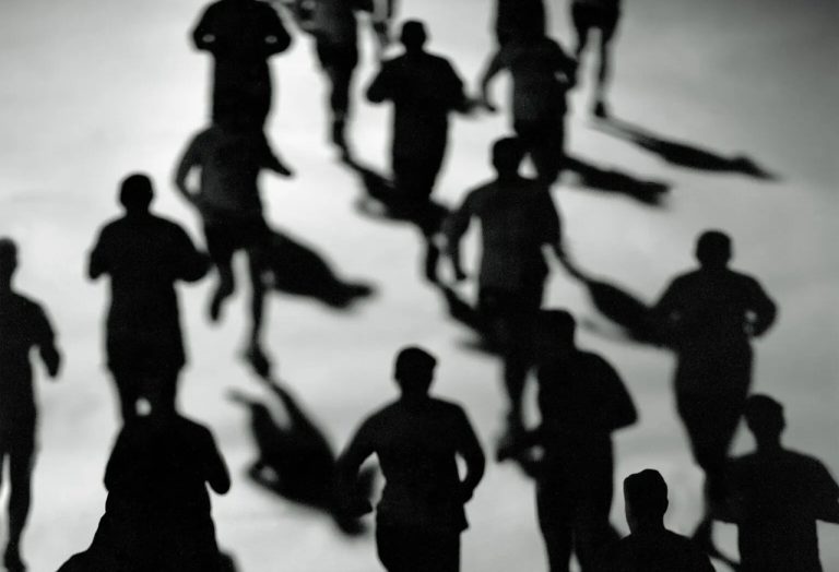 High-angle black and white silhouette of multiple runners moving together.