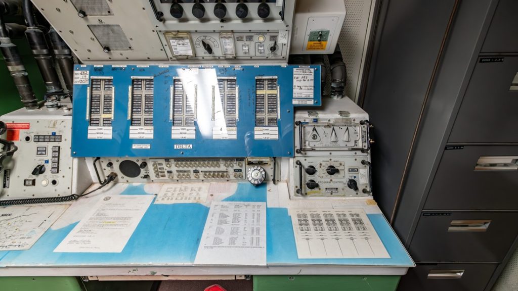 Vintage control panel desk with analog switches, dials, and technical operational manuals.