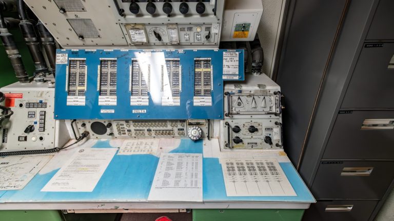 Vintage control panel desk with analog switches, dials, and technical operational manuals.