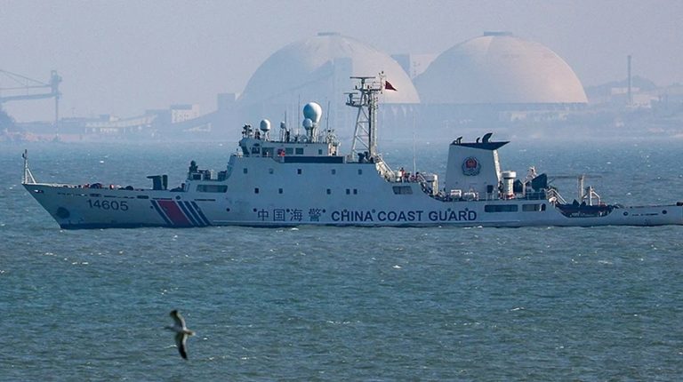 China Coast Guard patrol vessel sailing in open water with industrial domes in the background