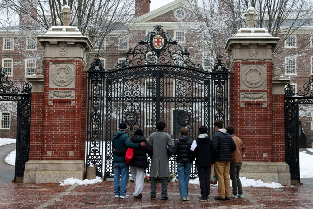 Group of seven students standing with their backs turned outside ornate iron campus gates in winter