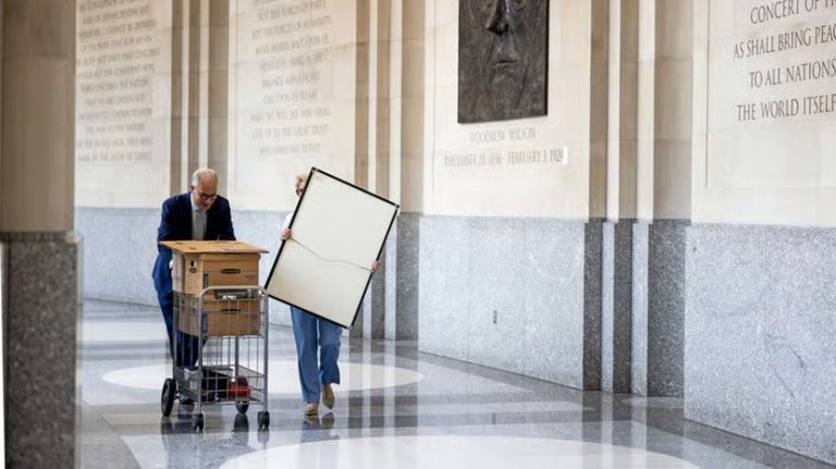 Government employees wheeling moving boxes and a whiteboard down a marble hallway