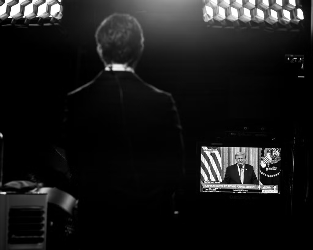 Black-and-white view of a broadcast studio monitor displaying Donald Trump speaking, framed from behind a silhouette.