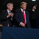 Donald Trump pointing forward while Kevin McCarthy claps on stage in front of an audience.