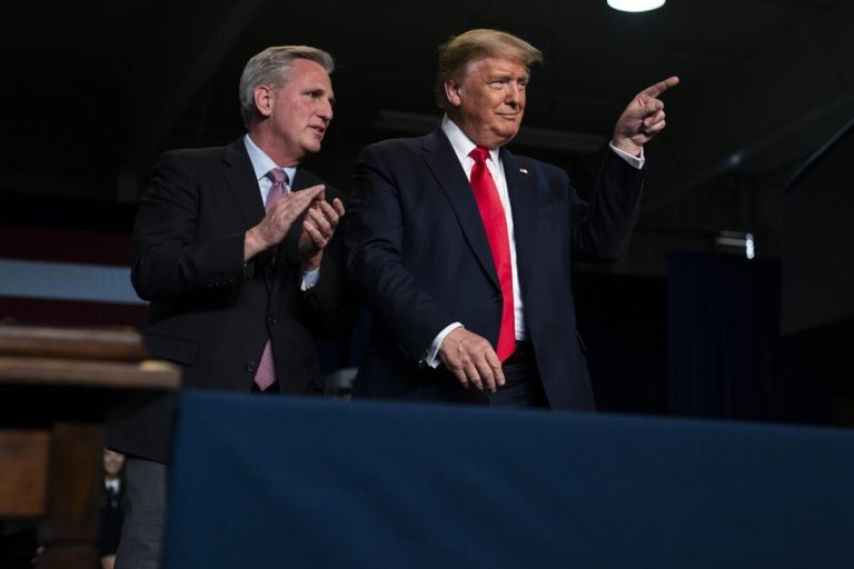 Donald Trump pointing forward while Kevin McCarthy claps on stage in front of an audience.