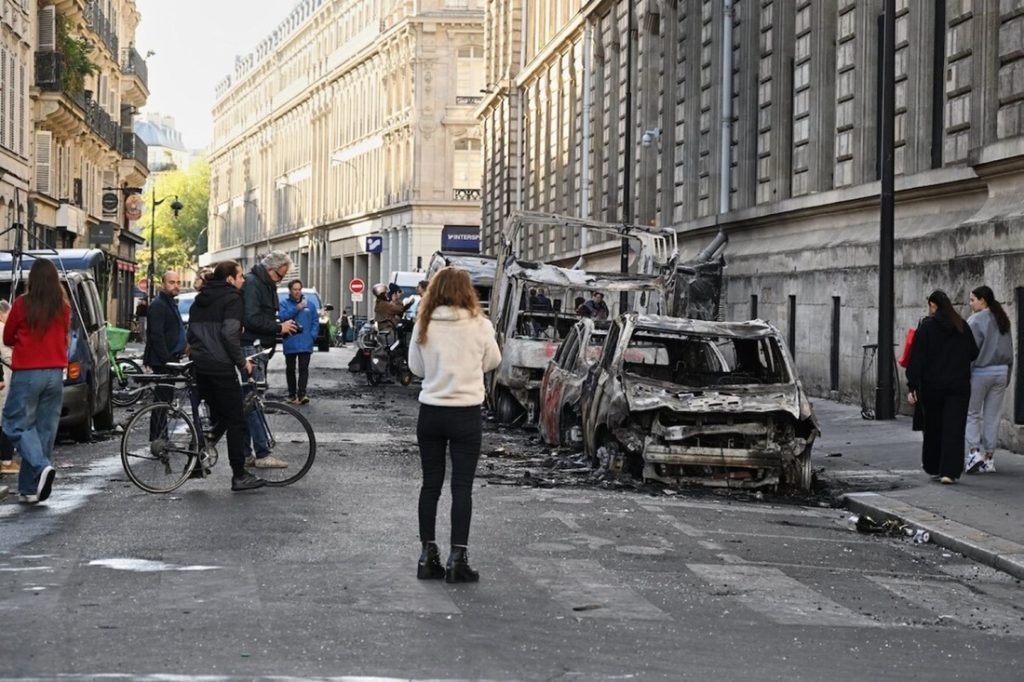 Burned vehicles and debris lining a street in Paris during public protests over economic and public service crises.